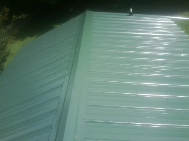 New green metal panels meeting at the ridge of a roof — Flat Roof Repair work by our crew in Kingston