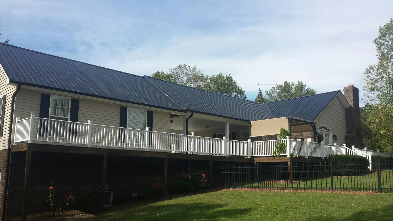 Black metal roof above a long white railed deck on a hillside home in Kingston